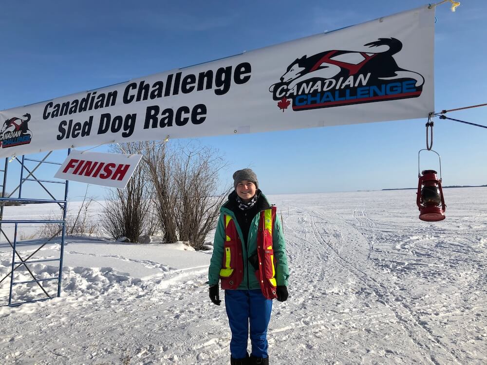 Staff member standing at the finish line of the Canadian Challenge Sled Dog Race, representing community involvement in Saskatoon